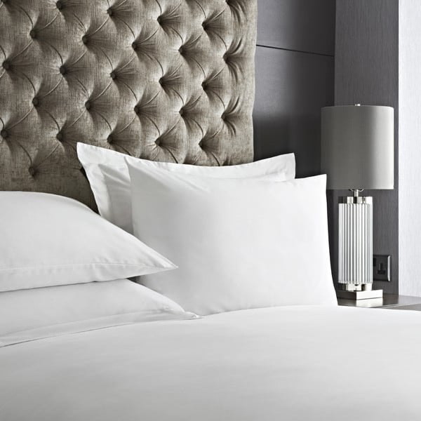 Crisp white cotton-rich bed linen on a hotel bed with a buttoned headboard