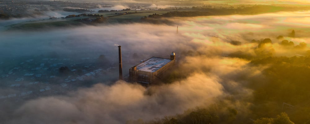 Aerial view of Kearsley Mill and its chimney rising through morning mist at sunrise