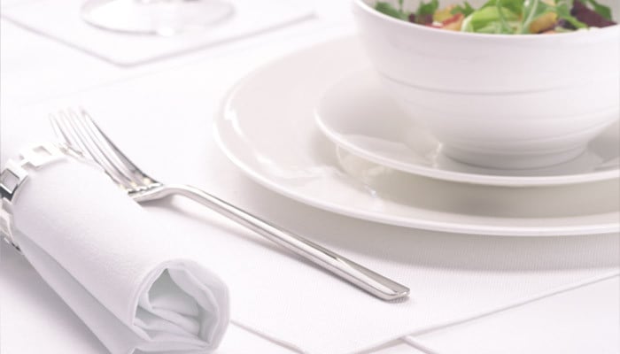 A restaurant table laid with crisp white table linen, napkin and place settings