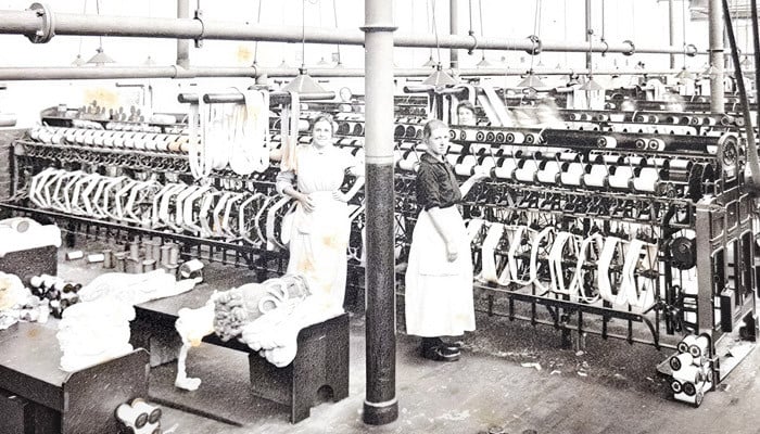 Two workers winding cotton from hanks to bobbins at rows of winding frames